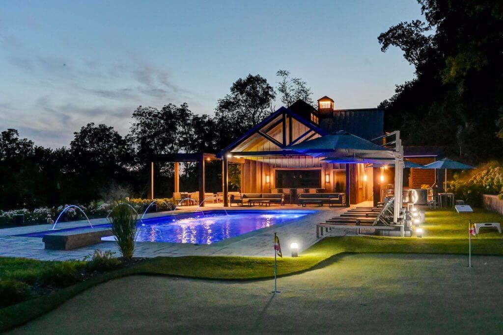 Pool house and pool lit at dusk beside a putting green